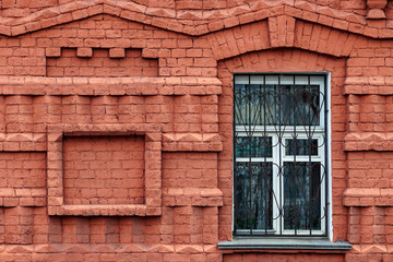 Fragment of the facade of an old building of curly red brick with a window