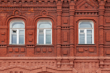 Fragment of the facade of an old building of curly red brick with three windows