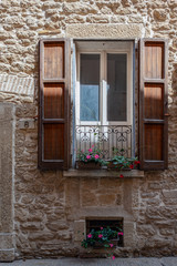Picturesque window of an old building with wooden shutters, a metal balcony and potted flowers
