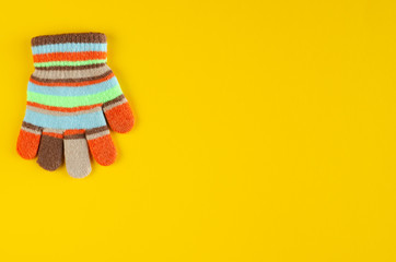 Striped kids winted gloves composition on yellow background.
