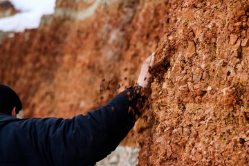 young man walks in  clay career in winter.  guy touches his hands with multi-colored layers of clay in  excavation.