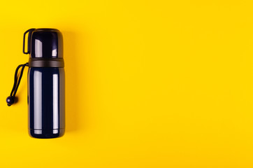 Dark thermos composition on yellow background. Flat lay