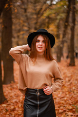 Autumn girl in the park. Sweater, hat and leather skirt. Stylish image. Atmosphere. Makeup