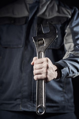 Professional construction worker shows a wrench on a dark background