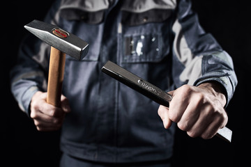Professional construction worker shows hammer and chisel on a dark background