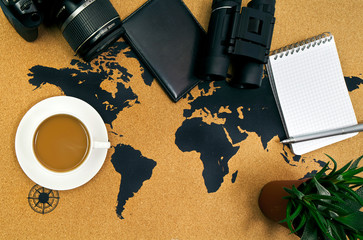 Cup of hot coffee on a map with camera, binoculars, passport, house plant, pen and notepad. Top view.