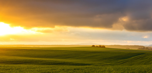 hazy rural evening landscape with golden light and grey hills in the background and field with...