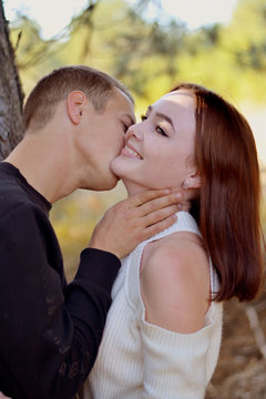 A young man kisses a beautiful laughing girl on the neck 