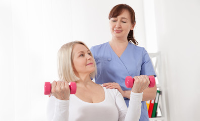 Modern rehabilitation physiotherapy. Physiotherapist helps an middle aged woman recover from an injury through exercise with dumbbells.