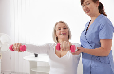 Modern rehabilitation physiotherapy. Physiotherapist helps an middle aged woman recover from an injury through exercise with dumbbells.