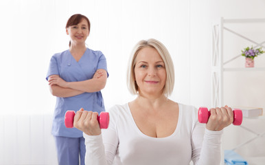 Picture of middle aged woman during rehabilitation in professional clinic. Rehabilitation, physiotherapy with dumbbells