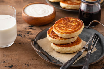 Homemade pancakes stack with milk and jam on wooden background.