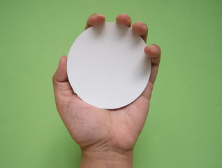 Woman hand holding white circle paper. Isolated in green background.
