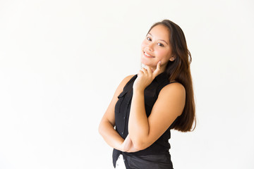 Fototapeta premium Happy carefree teenage girl touching face with finger, smiling at camera. Young Latin woman in casual standing isolated over white background. Positive emotion concept