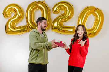 handsome couple man and woman with christmas present in front of 2020 new year balloons