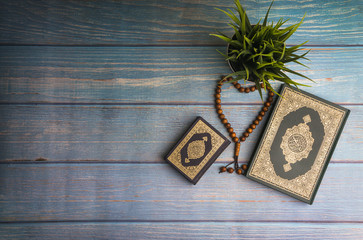 Flat lay view of vase, tasbih or rosary beads and Holy book of Quran with arabic calligraphy meaning of Al Quran over wooden paper background. Selective focus and crop fragment