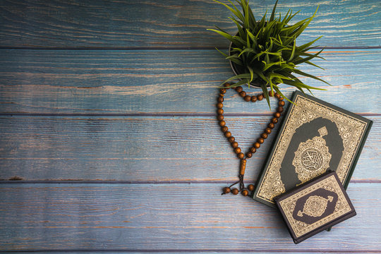 Flat lay view of vase, tasbih or rosary beads and Holy book of Quran with arabic calligraphy meaning of Al Quran over wooden paper background. Selective focus and crop fragment