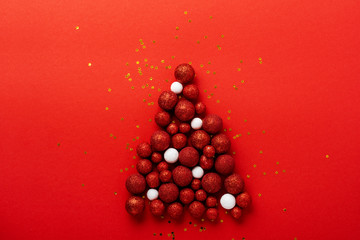 Christmas greeting card with Christmas tree made of red toys balls decorated golden confetti in red envelope on red background. New year concept. Top view