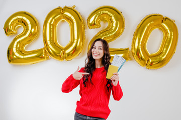 woman in red sweater holding template airplane  tickets with passport in front of 2020 new year balloons