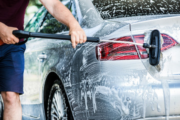 Car washing with brush and foam rear light on luxury vehicle.