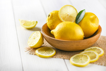 Fresh ripe yellow lemon in wooden bowl with green leaf on white table.  Healthy slices fruits on rustic board.