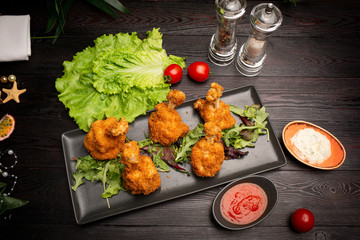 breaded chicken wings with spicy sauce and herbs on a black board