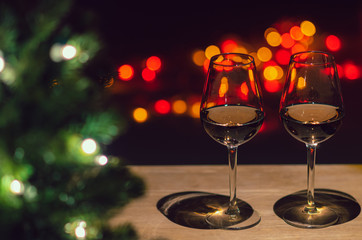 Two glasses of Rose wine on wooden table with Christmas tree and colorful bokeh light background.