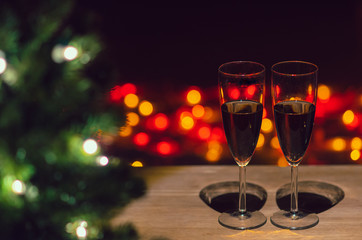 Two glasses of Rose wine on wooden table with Christmas tree and colorful bokeh light background.