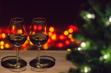 Two glasses of Rose wine on wooden table with Christmas tree and colorful bokeh light background.