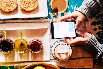 Above close up view of people doing healthy breakfast while answer messages on mobile phone -chat activity on device at home or hotel -  internet addiction concept and work