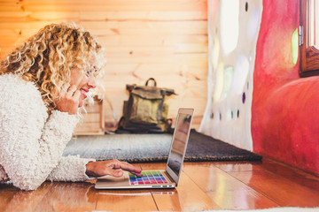 Cheerful nice caucasian young woman work and write on personal laptop computer laying on the wooden...