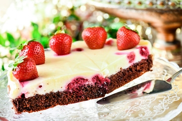 Delicious strawberries tart with vanilla cream on top. Chocolate cake and silver dessert scoop on glass tray with glitters in background.