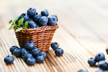Fresh finest blueberries in small wicker basket. Few blueberry sprinkled or leaved on rustic table.