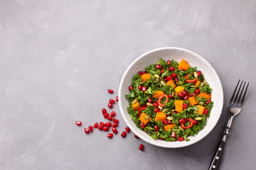Plate of kale salad, baked pumpkin, pumpkin seeds and pomegranate on gray background, top view. healthy diet food