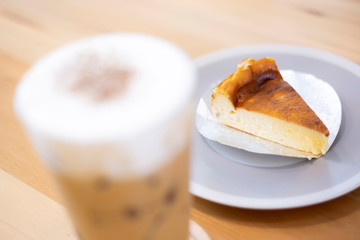 Close-up cheesecake sliced in white dish on wooden table background with glass of ice coffee. Coffee break time relaxation after meeting.