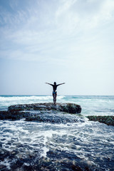 Woman practice yoga at the seaside cliff edge facing the coming strong sea waves