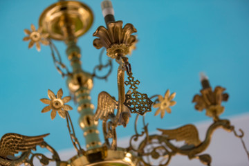Gold candlestick chandelier with azure ceiling in the background.