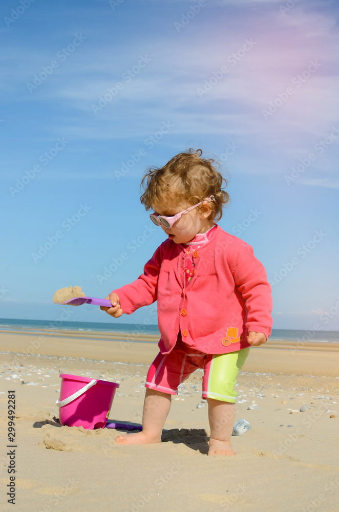 Poster pretty little girl playing on the beach and protected from the sun