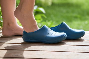 Young Barefoot girl puts rubber boots on standing on the porch of a country house in summer morning