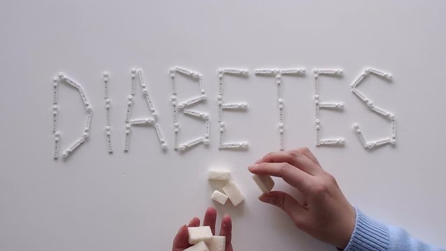 The word DIABETES with lancets for glucometer on the table on a white background. Lay next to the sugar cubes. A woman's hand takes a sugar cube. The concept of type 1 and type 2 diabetes.