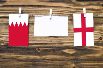 Hanging flags of Bahrain and England attached to rope with clothes pins with copy space on white note paper on wooden background.Diplomatic relations between countries.