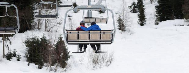 Naklejka premium Two skiers on chair-lift in gray day