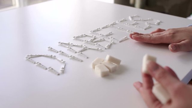 The word DIABETES with lancets for glucometer on the table on a white background. Lay next to the sugar cubes. A woman's hand takes a sugar cube. The concept of type 1 and type 2 diabetes.