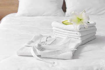 Soft clean bathrobe and towels on bed