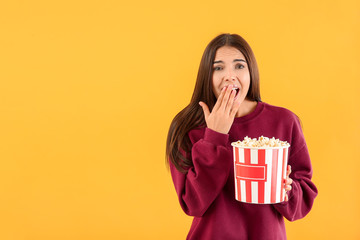 Afraid woman with popcorn on color background