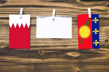 Hanging flags of Bahrain and Guadeloupe attached to rope with clothes pins with copy space on white...