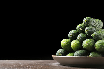 Plate with fresh green cucumbers on table against dark background