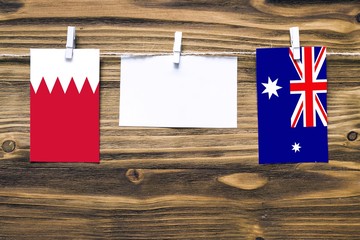 Hanging flags of Bahrain and Heard and Mcdonald Islands attached to rope with clothes pins with copy space on white note paper on wooden background.Diplomatic relations between countries.