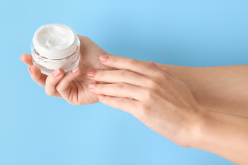 Female hands with jar of cream on color background