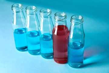 One bottle with red liquid among bottles with blue samples on color background. Concept of uniqueness